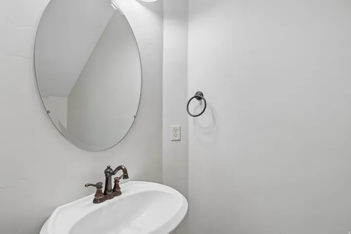 Pedestal sink with oil-rubbed bronze faucet, oval mirror, and wall-mounted towel ring