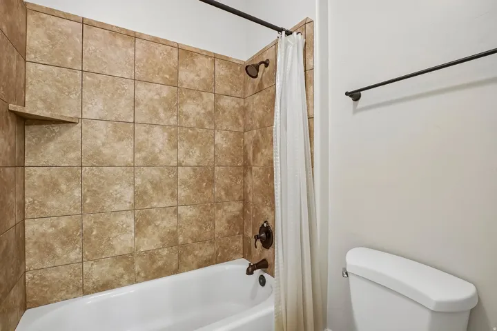Bathtub and shower combination featuring earth-toned wall tiling with a built-in shelf, bronze fixtures, and a shower curtain rod