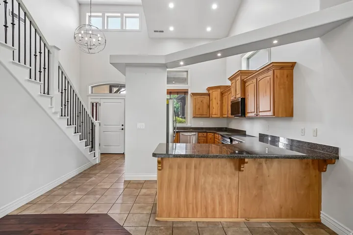 Open-concept interior featuring a kitchen with wood cabinetry and dark countertops, an integrated breakfast bar, and stainless steel appliances