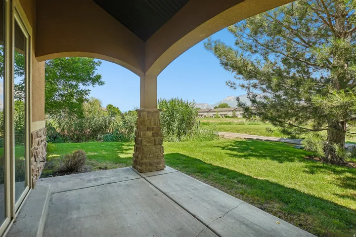 Covered patio with concrete flooring, stone-clad columns, and a stucco exterior