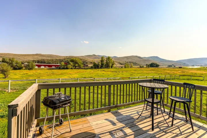 Expansive wooden deck with a slatted railing overlooking a vast landscape featuring rolling hills and green fields