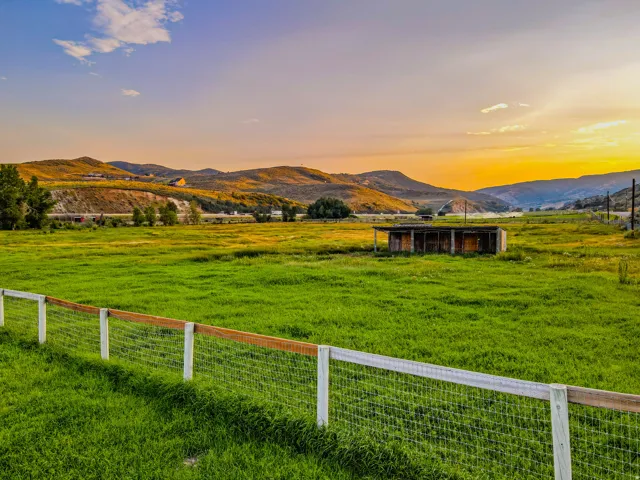 Expansive green field with a wire and wood-post fence and horse shelter