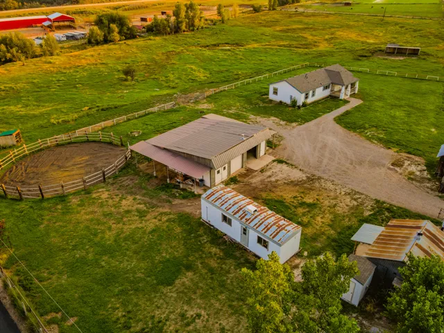 Expansive property featuring a single-story residence, a large detached shop/garage with an extended metal roof, and a fenced round pen