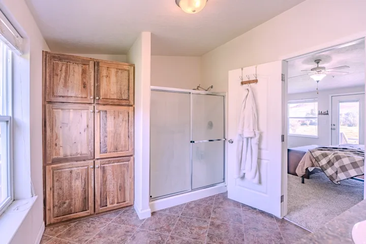 Built-in wood-finish cabinetry, tile flooring, glass-enclosed shower, ceiling fan, and outdoor access