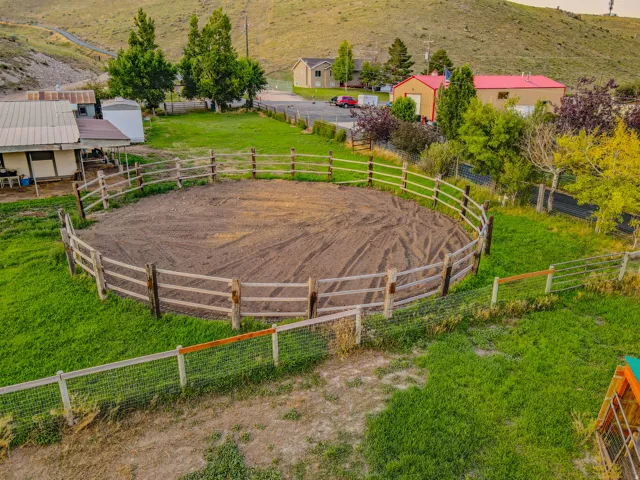 Outdoor riding arena with wood fencing, surrounded by green grass and mature trees