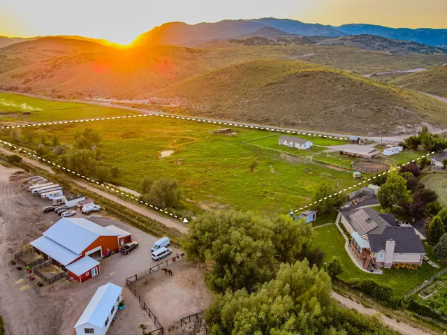 Expansive acreage featuring a traditional residence with solar panels, a large red barn, multiple outbuildings, and fenced paddocks