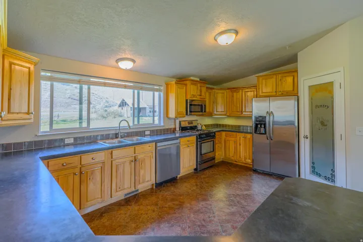 Kitchen featuring wood cabinetry, stainless steel appliances, dark countertops, tile backsplash, and wood-finish flooring