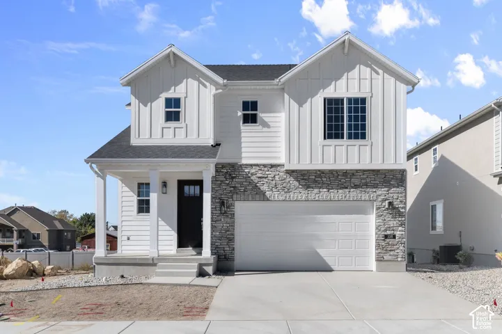 Two-story exterior featuring white board-and-batten siding, stone veneer accents, an attached two-car garage, and a covered front porch entry