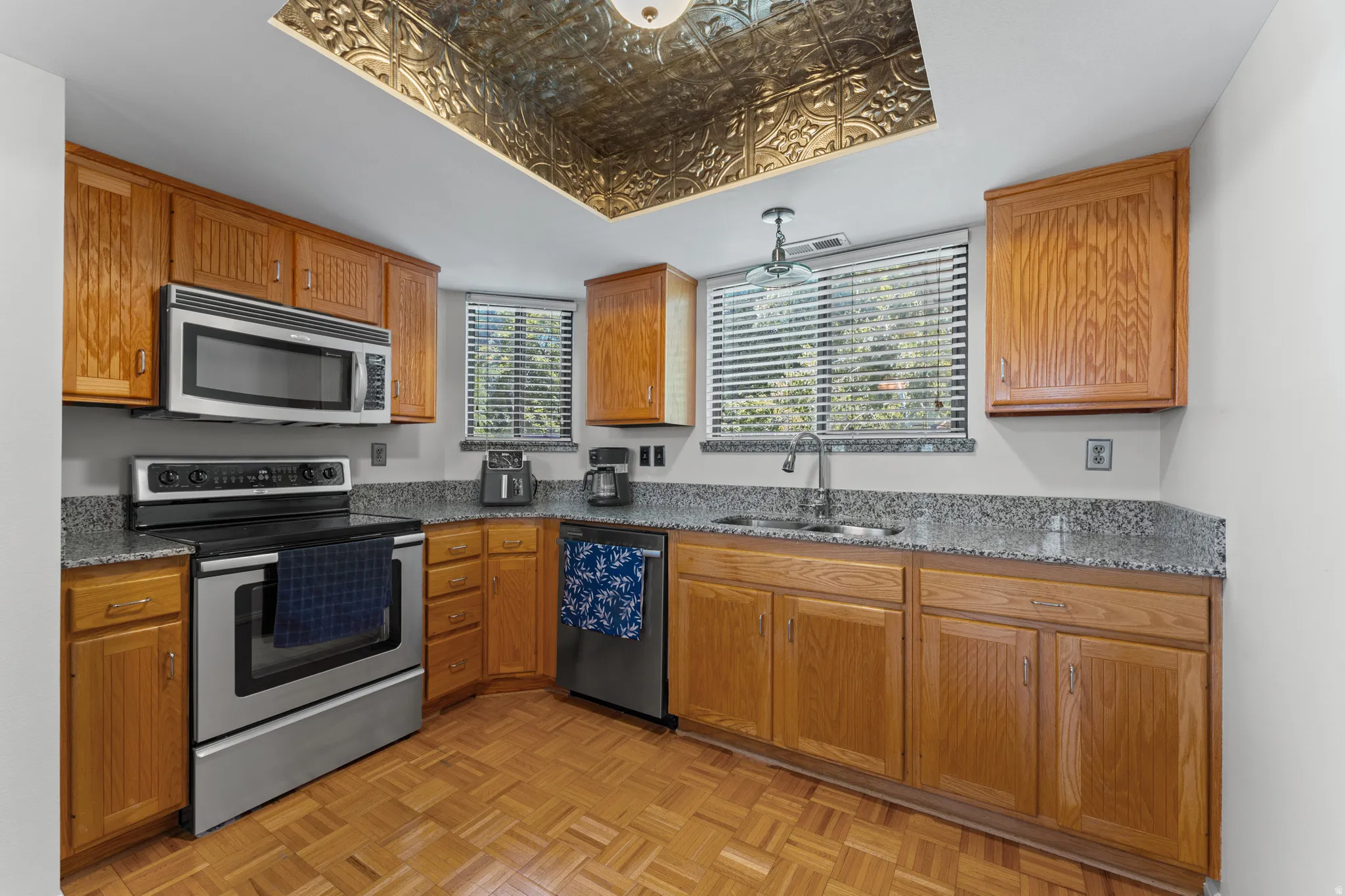 Kitchen featuring wood cabinetry, stainless steel appliances, granite-style countertops, wood-finish flooring, and a decorative ceiling panel