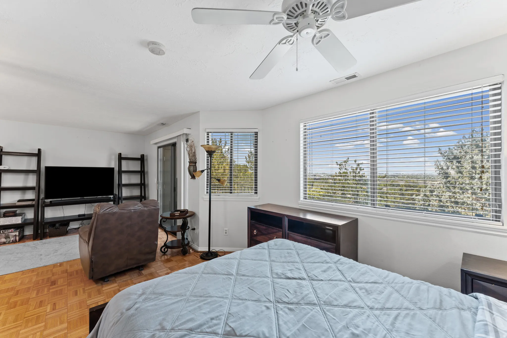 Bright room featuring expansive windows with white blinds, wood-finish parquet flooring, and a ceiling fan