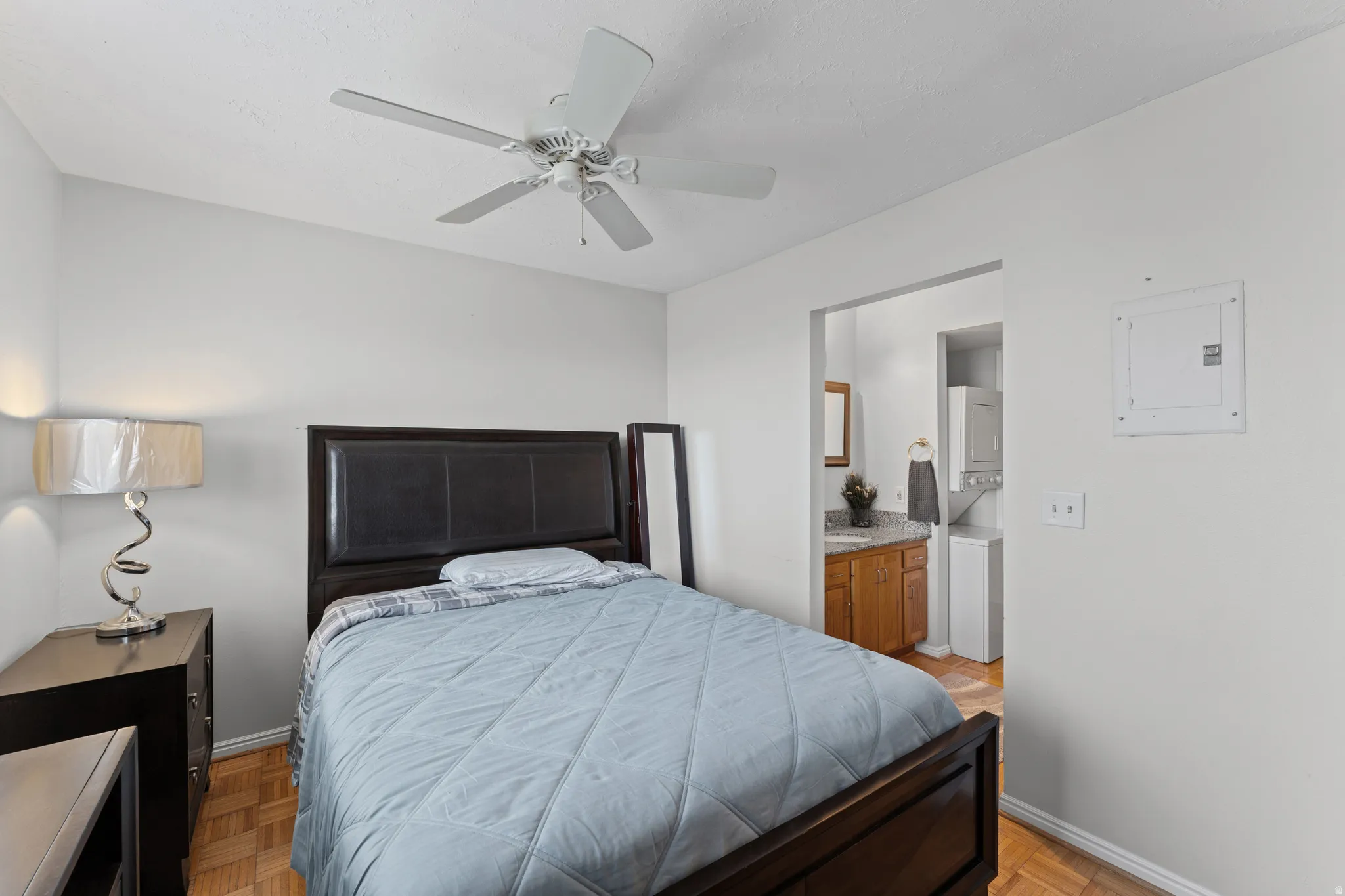 Bedroom featuring wood-finish flooring, a ceiling fan, and access to an adjacent utility area with a stacked appliance