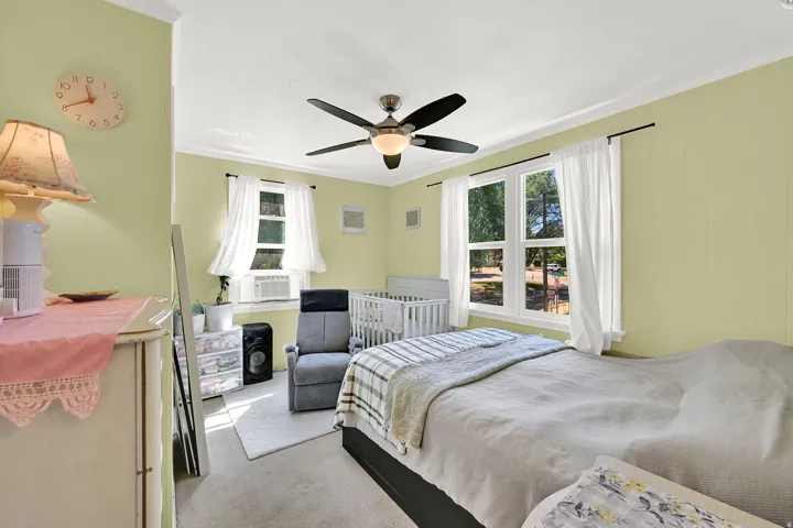 Spacious room featuring light green paneling, crown molding, two windows with white trim, and a ceiling fan with integrated lighting