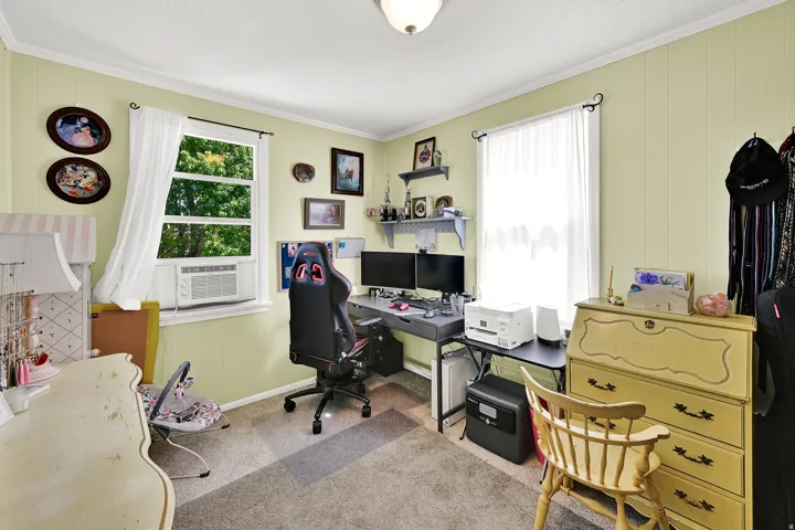 Bedroom featuring two windows with white trim, carpeting, and light green vertical paneling on some walls