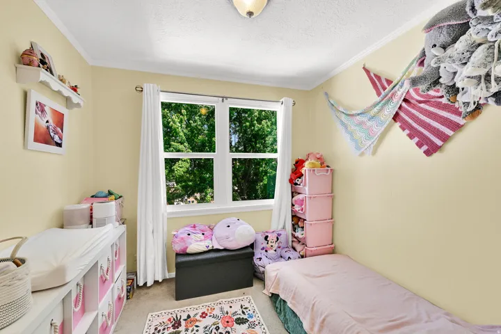 Bright and cheerful bedroom featuring soft yellow walls, large multi-pane windows with white trim flooding the space with natural light, and hardwood flooring