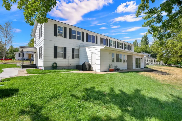 Classic two-story colonial with white exterior siding and black shutters, featuring a spacious front lawn with mature landscaping and shade trees