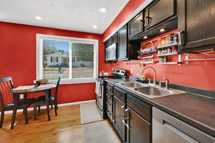 Vibrant kitchen featuring bold red walls, dark wood cabinetry with under-cabinet lighting, stainless steel appliances, and a dual-basin sink with chrome faucet