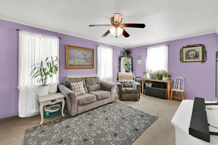 Spacious living room featuring soft purple walls, recessed ceiling fan with brushed metal finish, and large windows with sheer curtains providing natural light