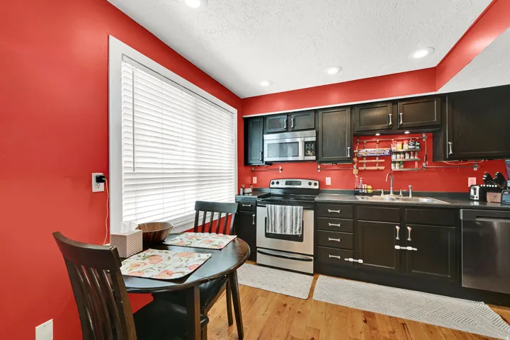 Kitchen featuring a window with white blinds, black cabinetry, stainless steel appliances, recessed ceiling lights, and wood-finish flooring