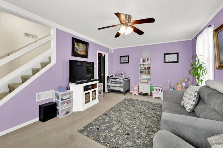 Spacious family room showcasing lavender accent walls, neutral carpet flooring, and ample natural light from multiple windows