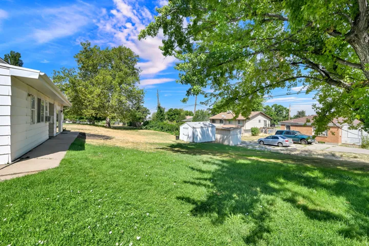 Expansive green lawn with mature shade trees and a concrete walkway leading to the property entrance