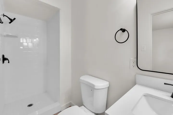 Bathroom featuring a white subway tile shower surround with matte black fixtures, a contemporary vanity with a white countertop and integrated sink, a matching matte black faucet, and a sleek black-framed mirror