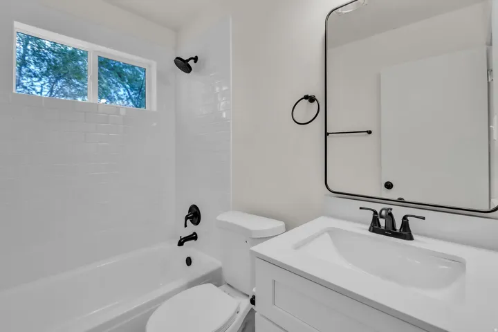 Bathroom featuring a white subway tile shower surround, matte black fixtures, a white vanity with integrated sink, and a framed mirror