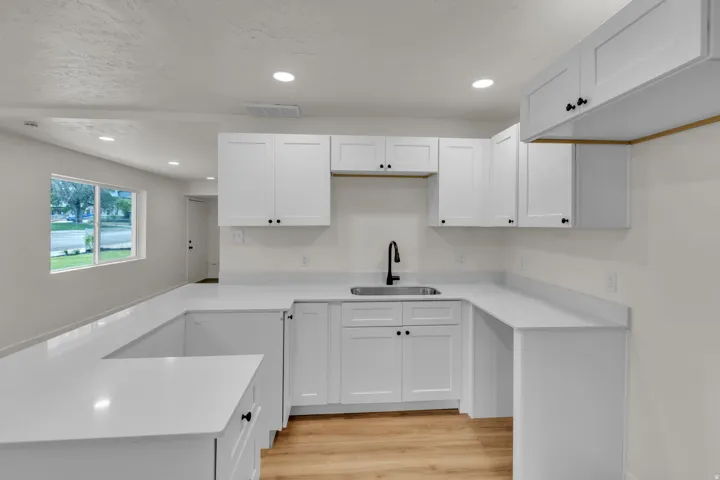 Modern kitchen featuring white shaker cabinetry, light-toned wood-finish flooring, recessed lighting, and a matte black faucet over a stainless steel sink