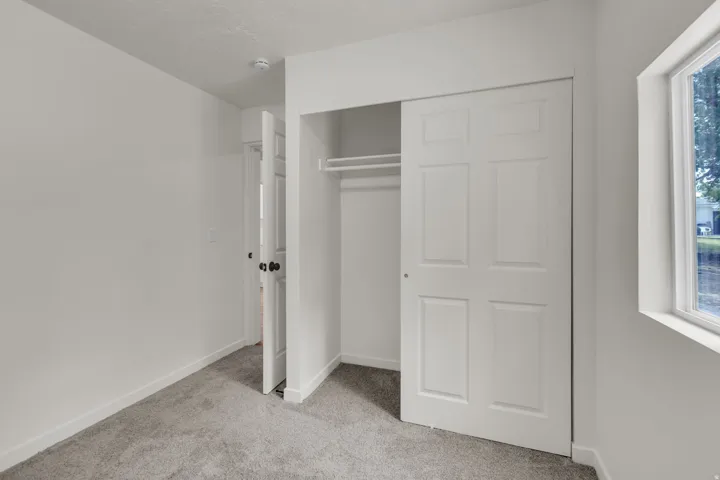 Neutral wall tones with gray carpeting, featuring a window, closet with sliding doors, and a paneled interior door