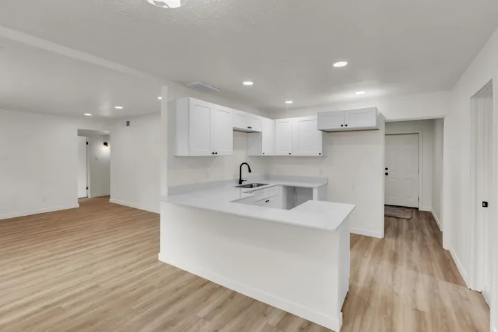 Open concept kitchen featuring white cabinetry, light-toned countertops, and a black faucet