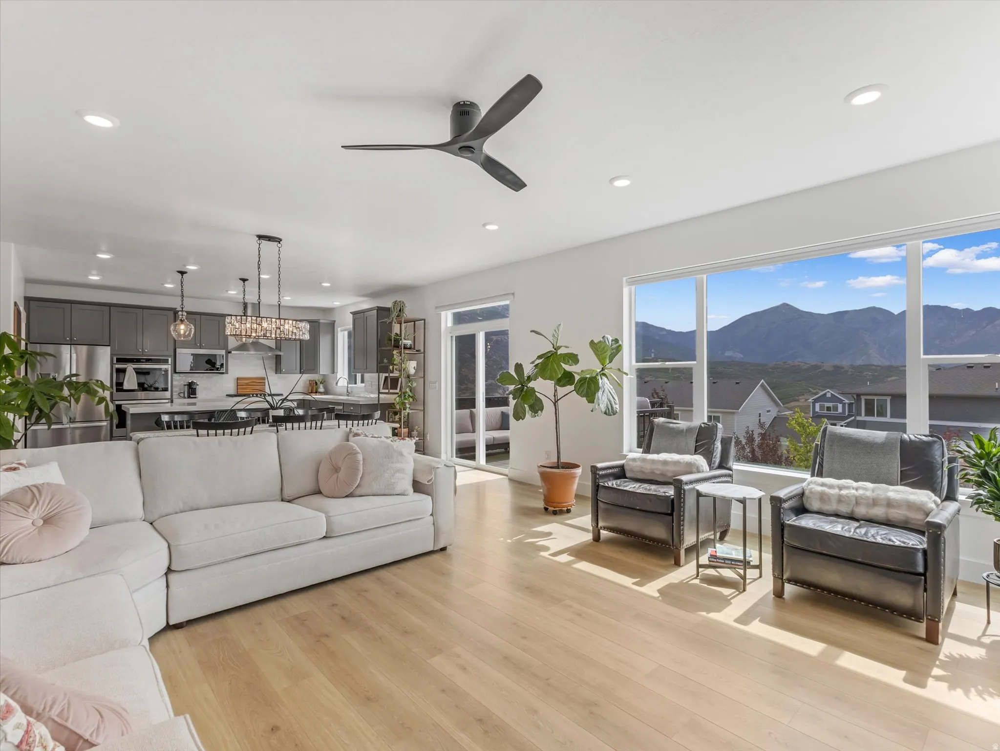 Expansive living area with large windows showcasing mountain scenery, light wood-finish flooring, recessed lighting, and a modern ceiling fan