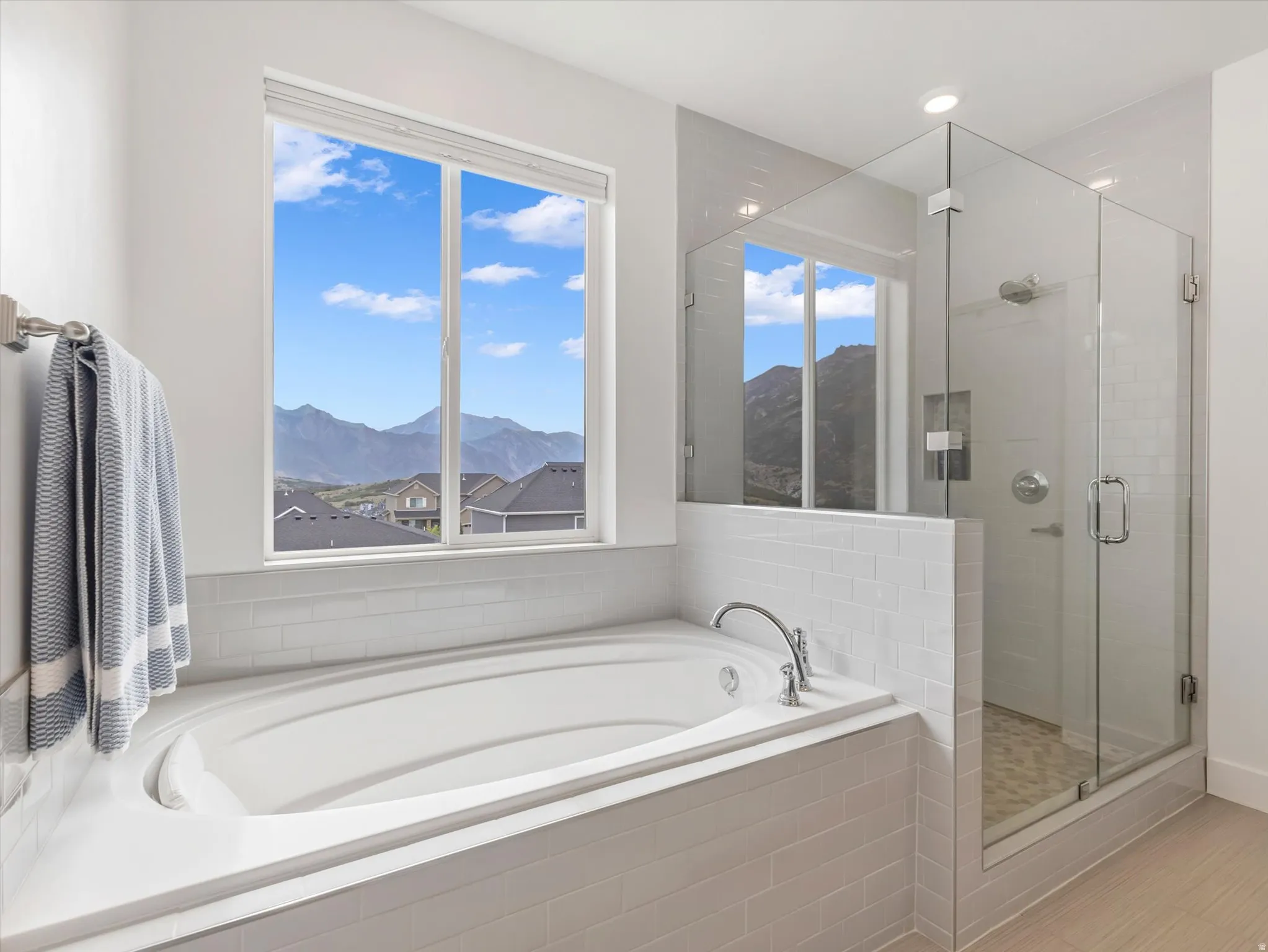 Soaking tub with a tiled surround, framed by a large window with mountain scenery