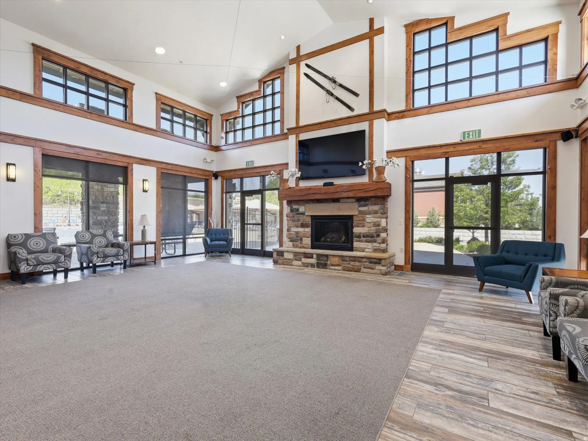 Spacious common area featuring a stone-clad fireplace with wood mantle, high ceilings, and large windows with dark frames