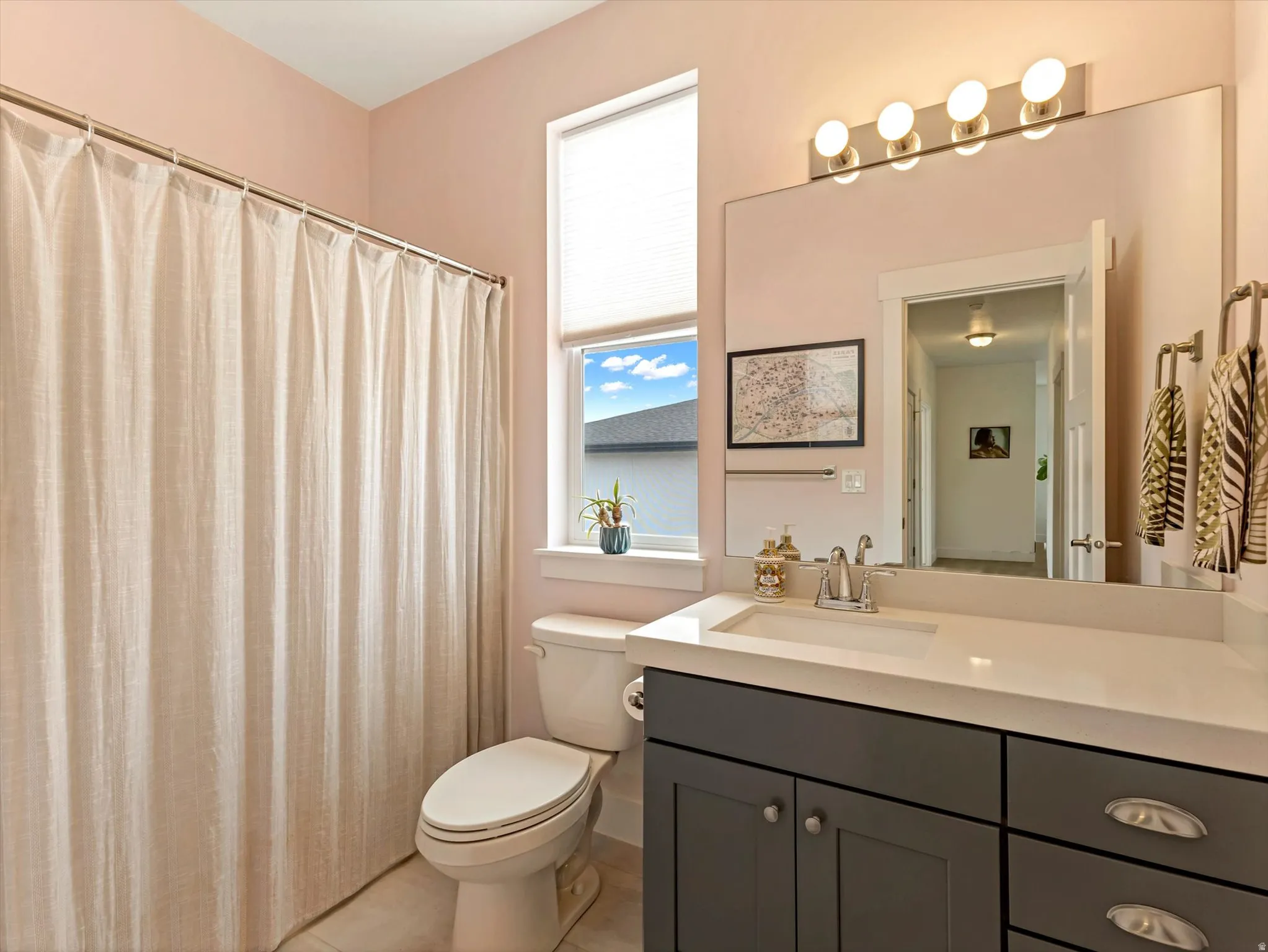 Bathroom featuring a single vanity with dark gray cabinetry and a light-toned countertop, an integrated sink with a chrome faucet, and a large wall-mounted mirror