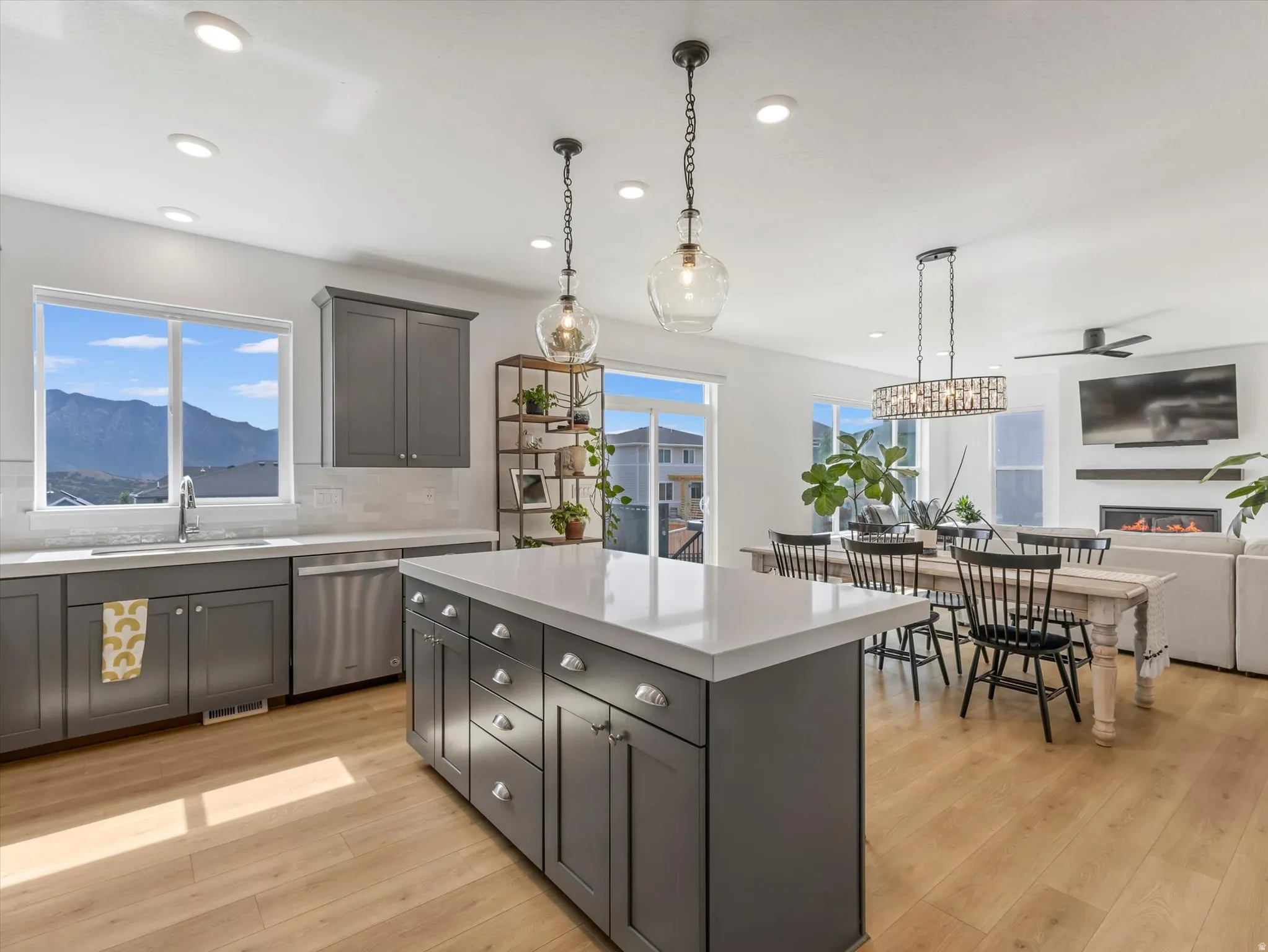 Modern kitchen featuring a large island with white countertops, gray cabinetry, stainless steel appliances, and wood-finish flooring