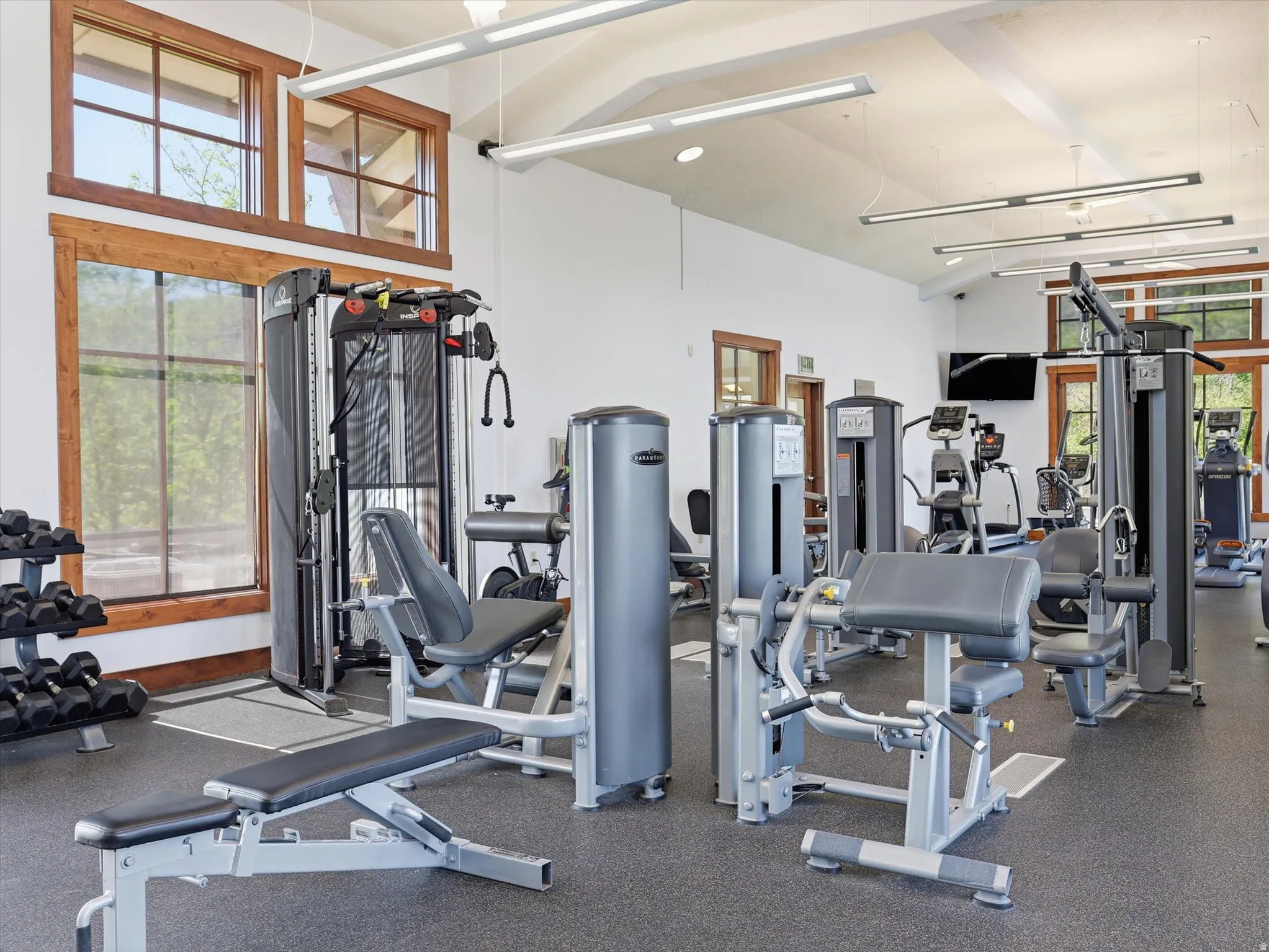 Fitness center featuring various exercise machines, high ceilings with exposed beams, wood-trimmed windows, and rubberized flooring