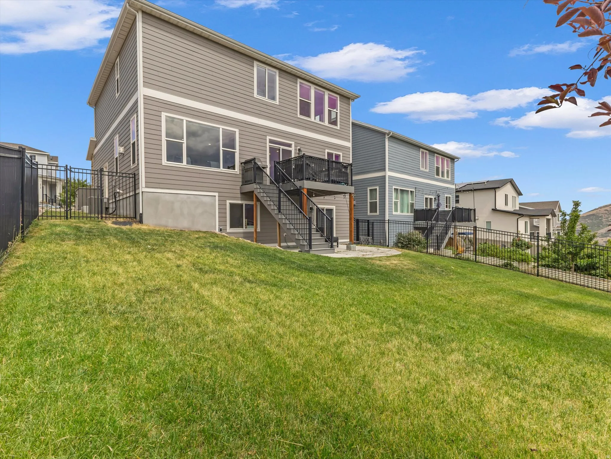 Sloping backyard featuring a manicured lawn, a black metal fence, and a multi-level deck with stairs