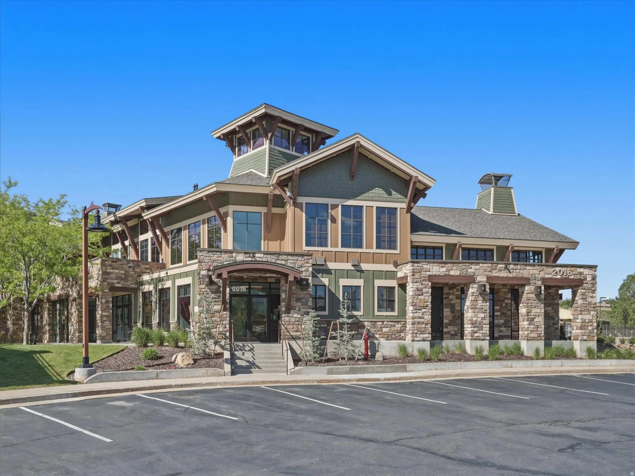 Multi-story building featuring stone and wood-look siding, extensive window treatments, a prominent central entrance, multiple rooflines, and a paved parking area