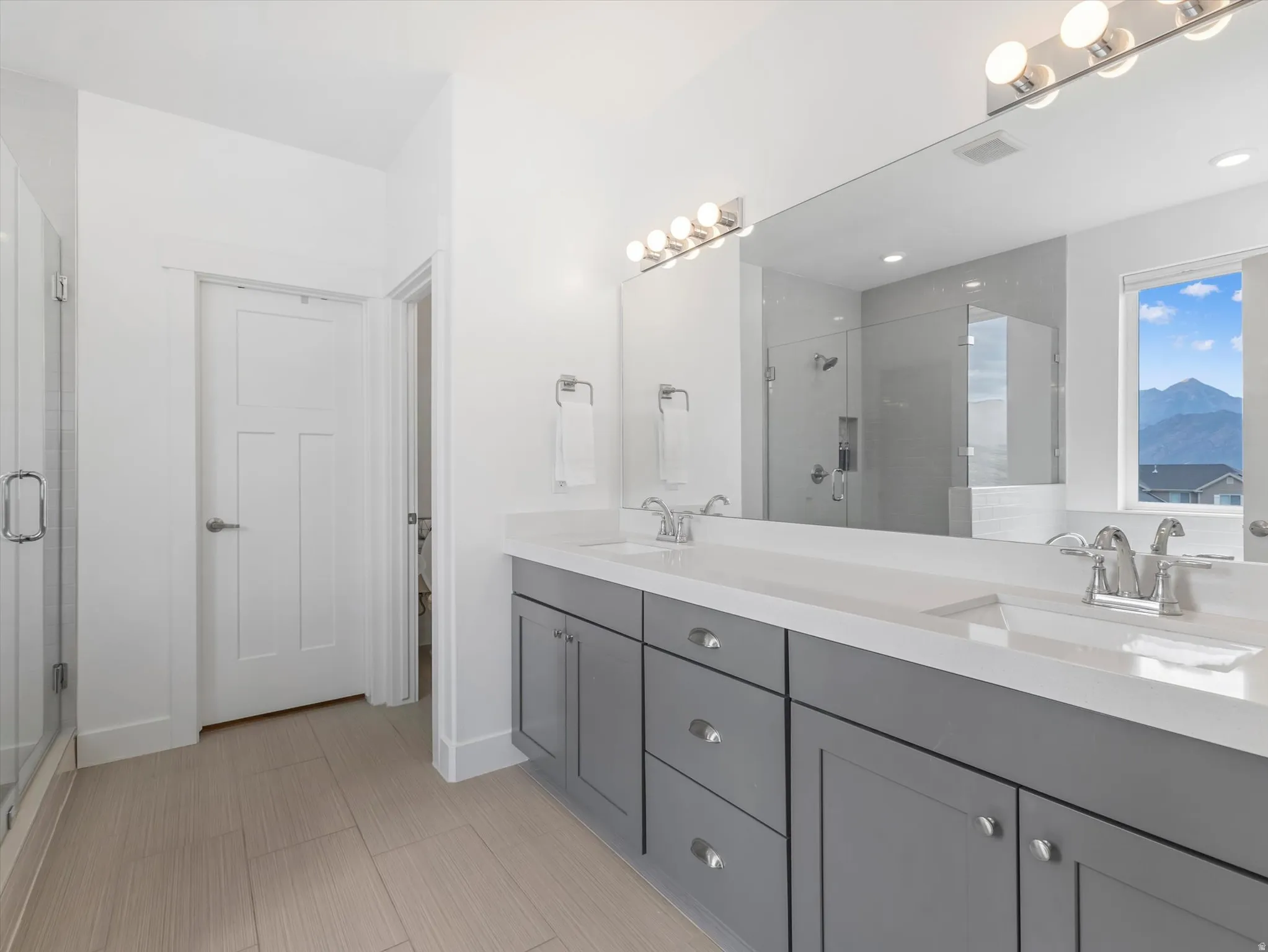 Bathroom featuring a double vanity with gray cabinetry, white countertops, and chrome fixtures