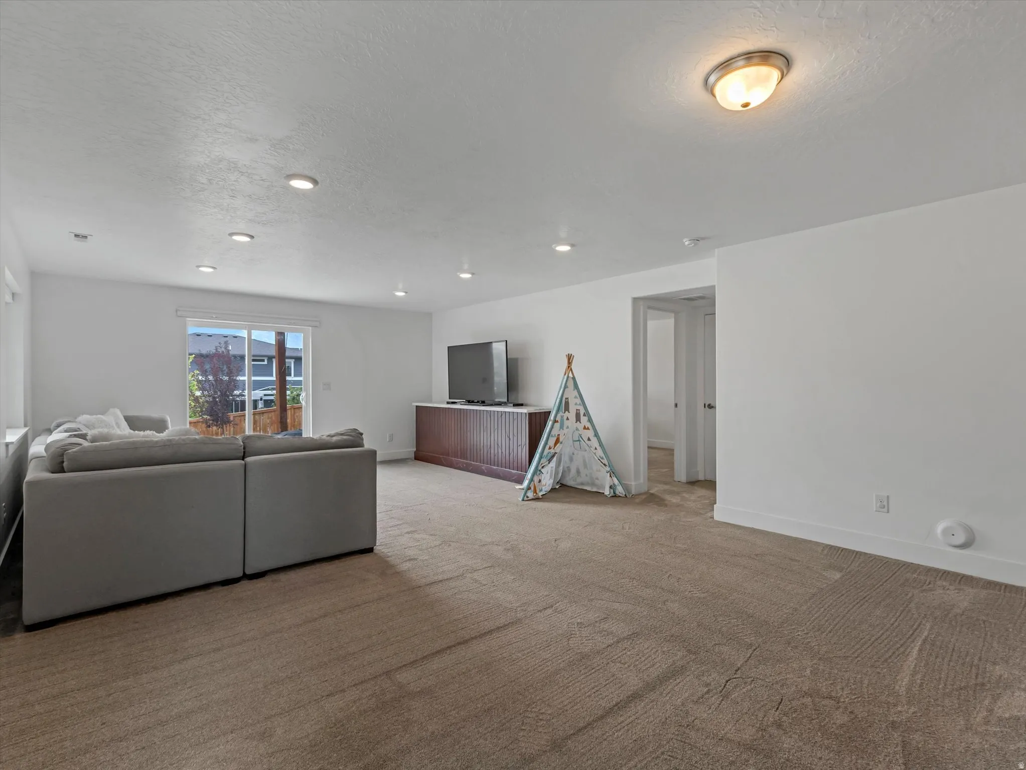 Spacious room featuring neutral carpeting, recessed lighting, and a sliding glass door providing exterior access