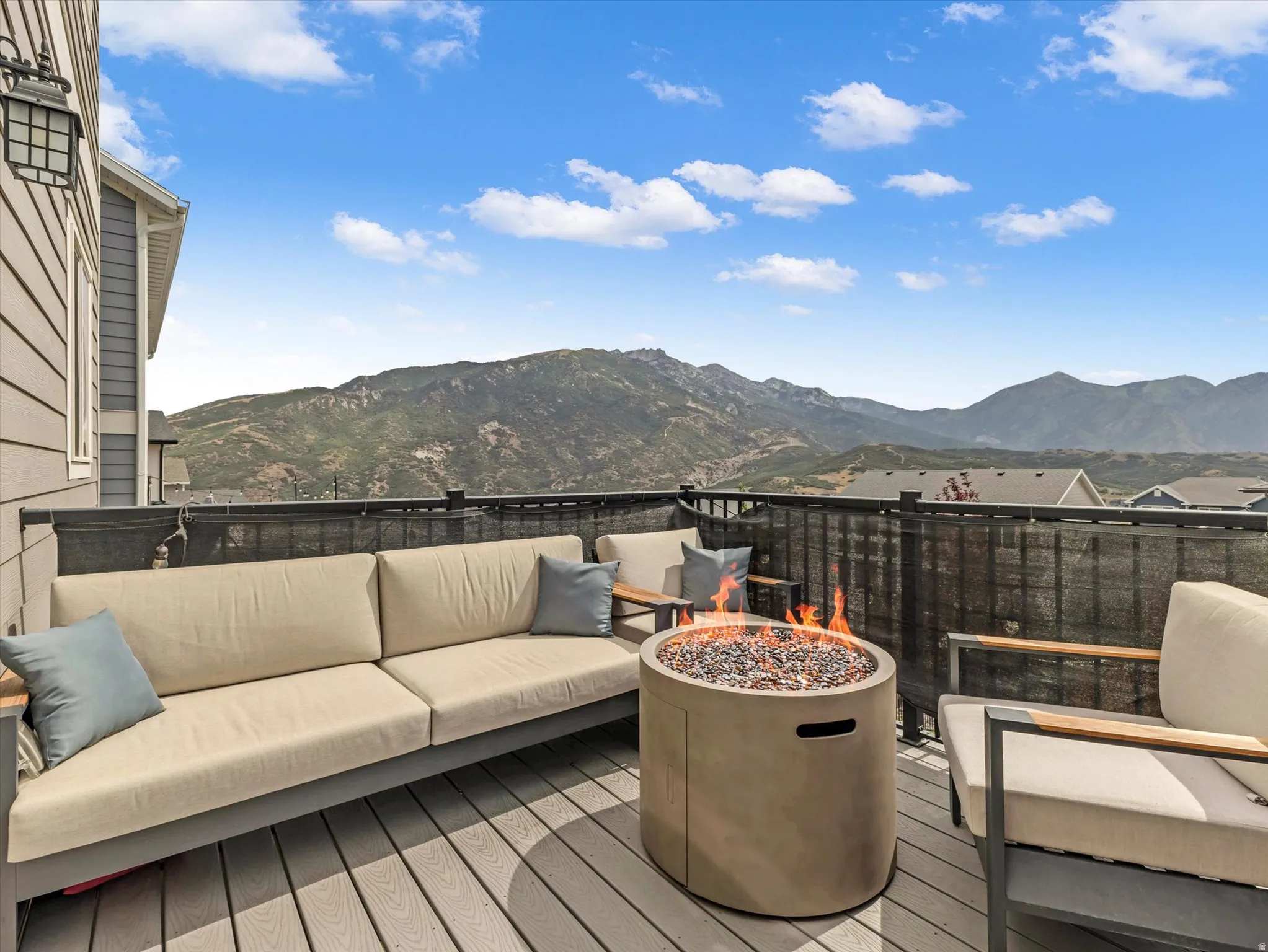 Expansive outdoor deck featuring composite decking, a mountain backdrop, black metal railings, and a built-in exterior light fixture