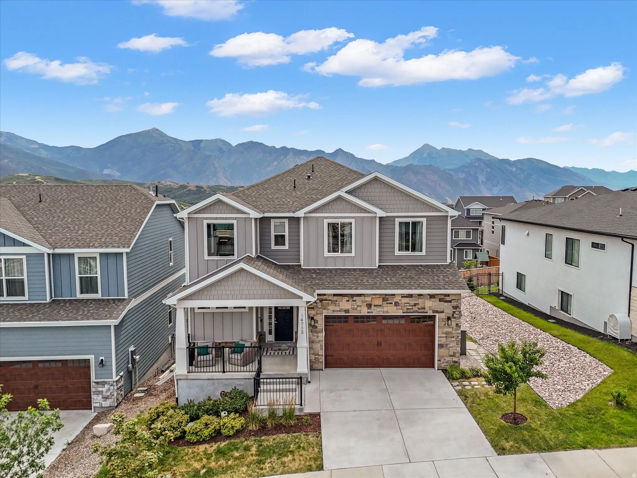 Contemporary two-story residence featuring a covered front porch, stone and siding exterior, two-car garage with wood-finish door, and concrete driveway