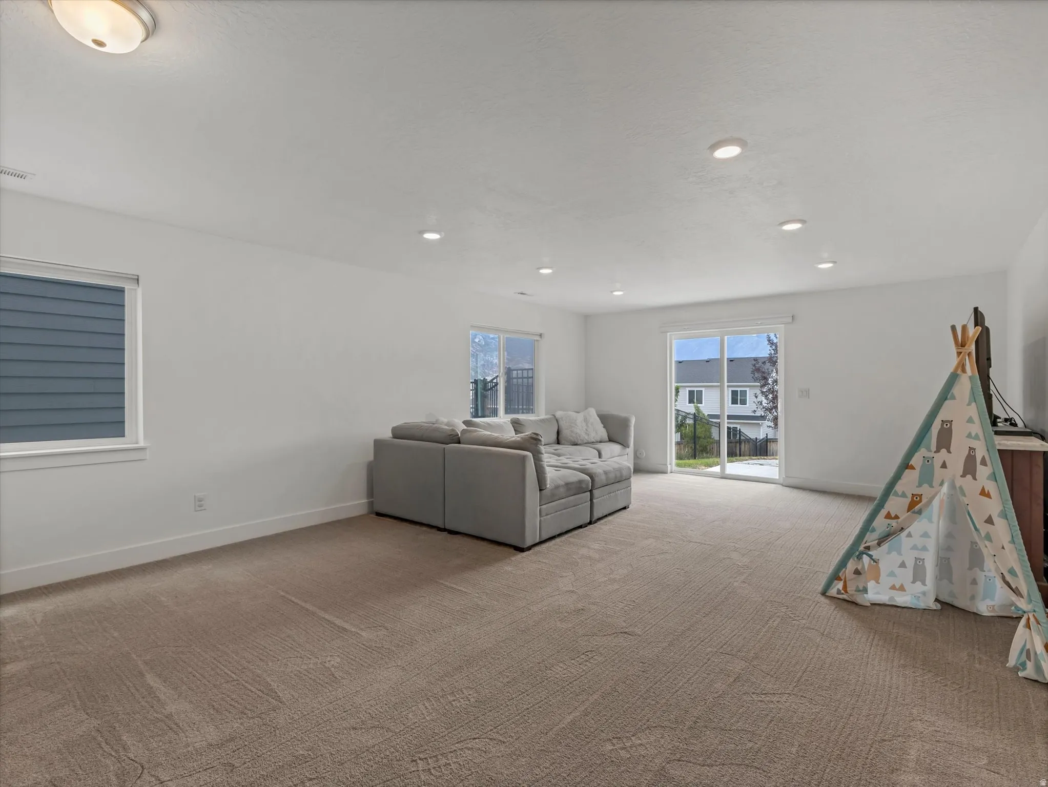 Spacious room featuring neutral carpeting, white walls, recessed ceiling lighting, and a sliding glass door providing outdoor access