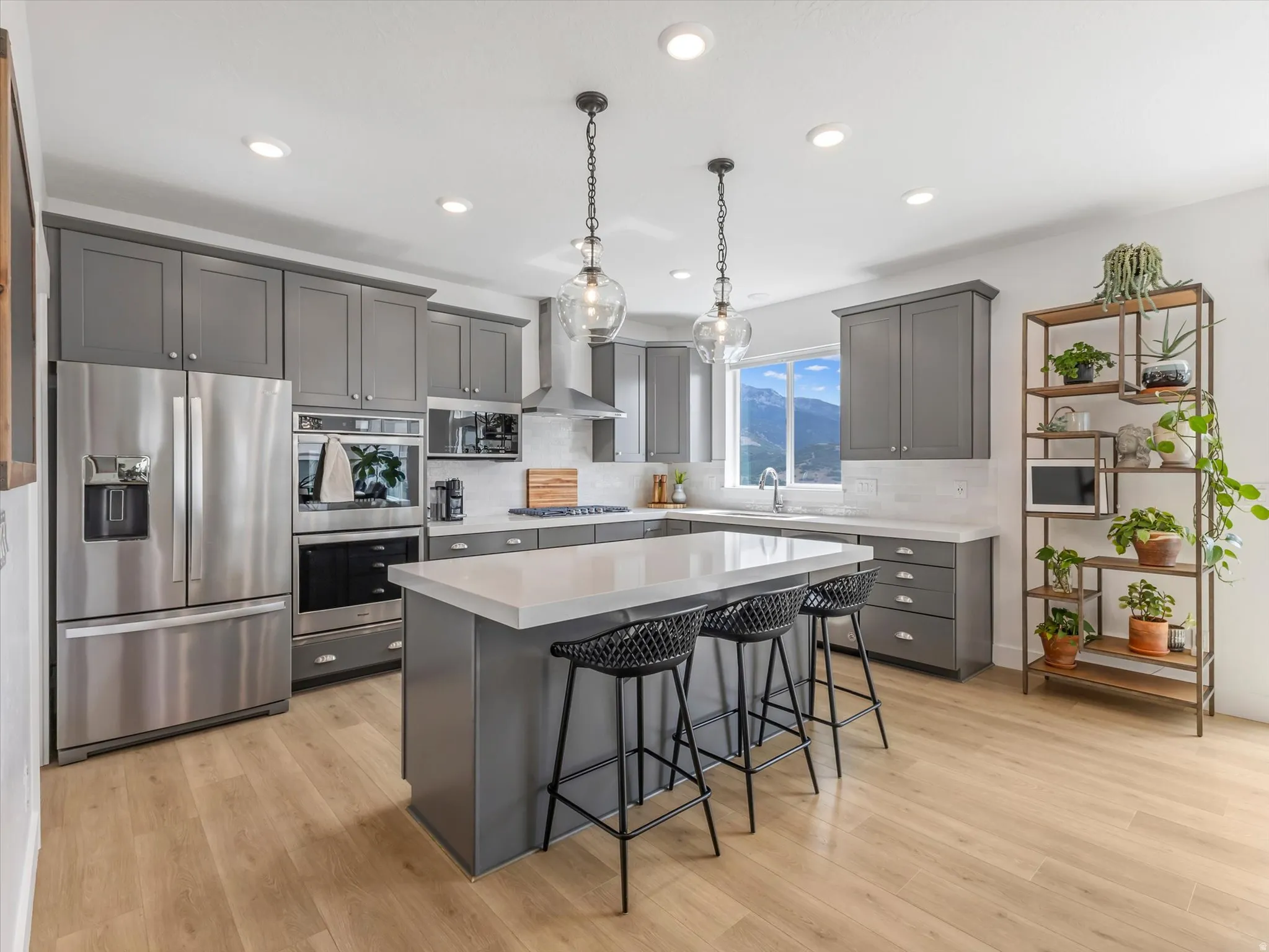 Contemporary kitchen featuring a central island with seating, stainless steel appliances, grey cabinetry, light wood-finish flooring, and recessed lighting
