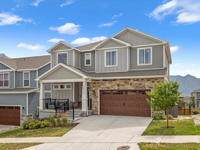 Contemporary two-story residence featuring a stone and siding exterior, an integrated two-car garage with wood-finish doors, a covered front porch, and a concrete driveway
