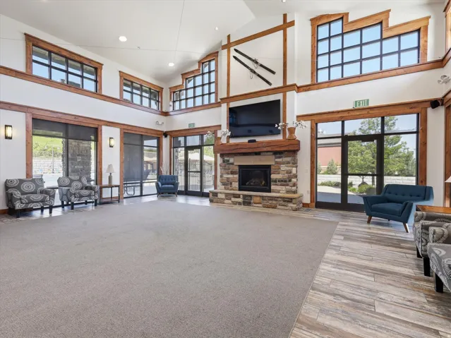 Spacious common area featuring a stone-clad fireplace with wood mantle, high ceilings, and large windows with dark frames