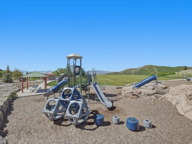 Community playground featuring multiple slides, climbing structures, a covered picnic area, and natural rock accents