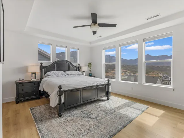 Spacious room featuring multiple large windows, light wood-finish flooring, a contemporary ceiling fan, and a tray ceiling detail