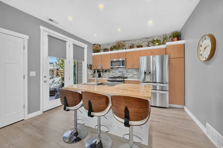 Modern kitchen featuring stainless steel appliances, light wood-finish cabinetry, a light wood countertop island, and light wood-finish flooring