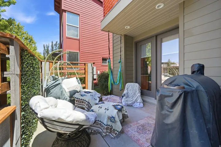 Paved outdoor patio featuring a privacy fence with artificial greenery, recessed lighting, and direct access through double glass doors
