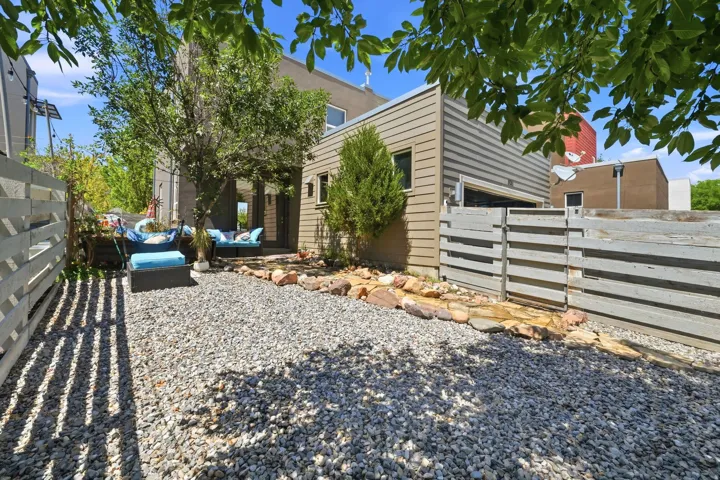 Gravel outdoor area featuring a mature tree, stone border, and horizontal slat fencing
